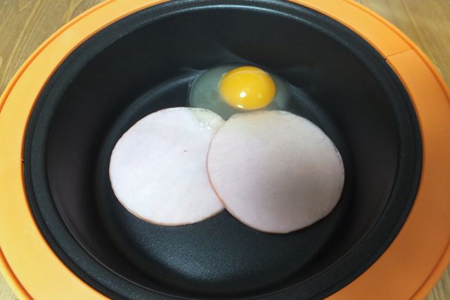 グリルクッカーにハム2枚を置き、卵を割り入れる。油を引かないのでフライパンで焼くよりヘルシーだ